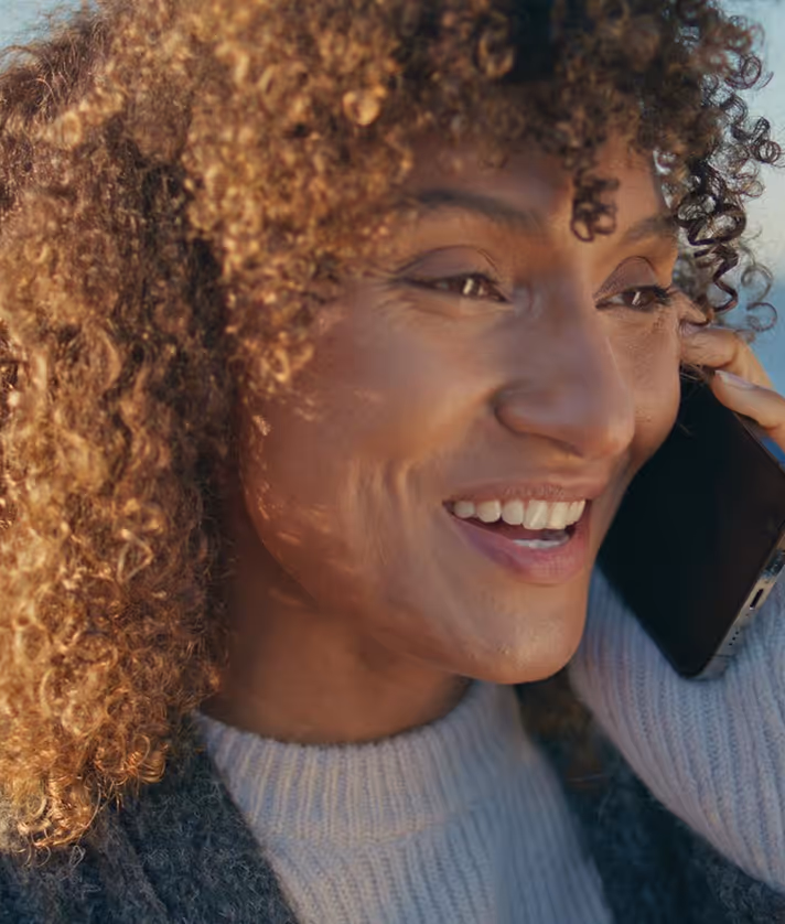 Close-up of a smiling woman with curly hair talking on a smartphone.