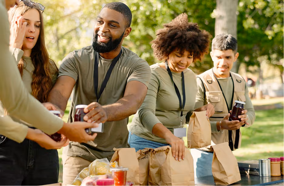 Volunteers packing food and beverages into paper bags outdoors at a community event.