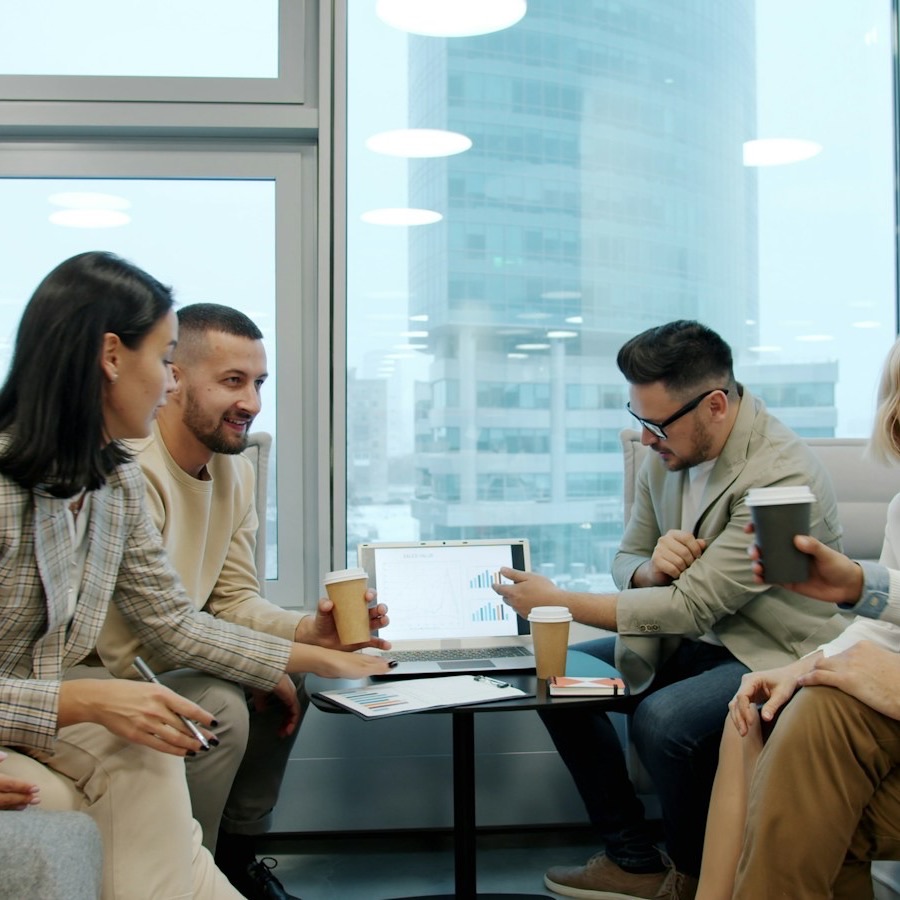 A small team talks over coffee around a laptop in a bright office