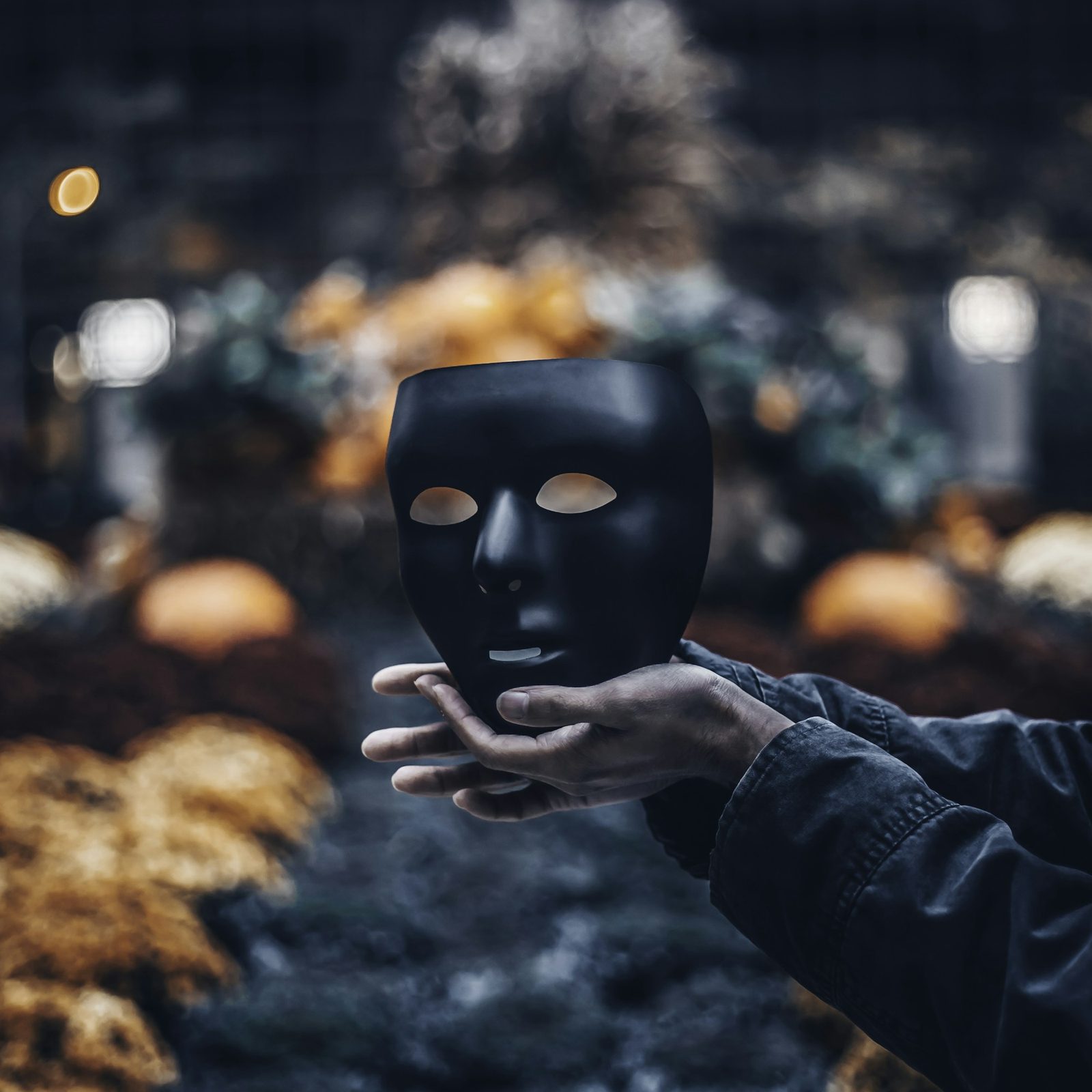A hand holding a mask away from a face, against an autumn background