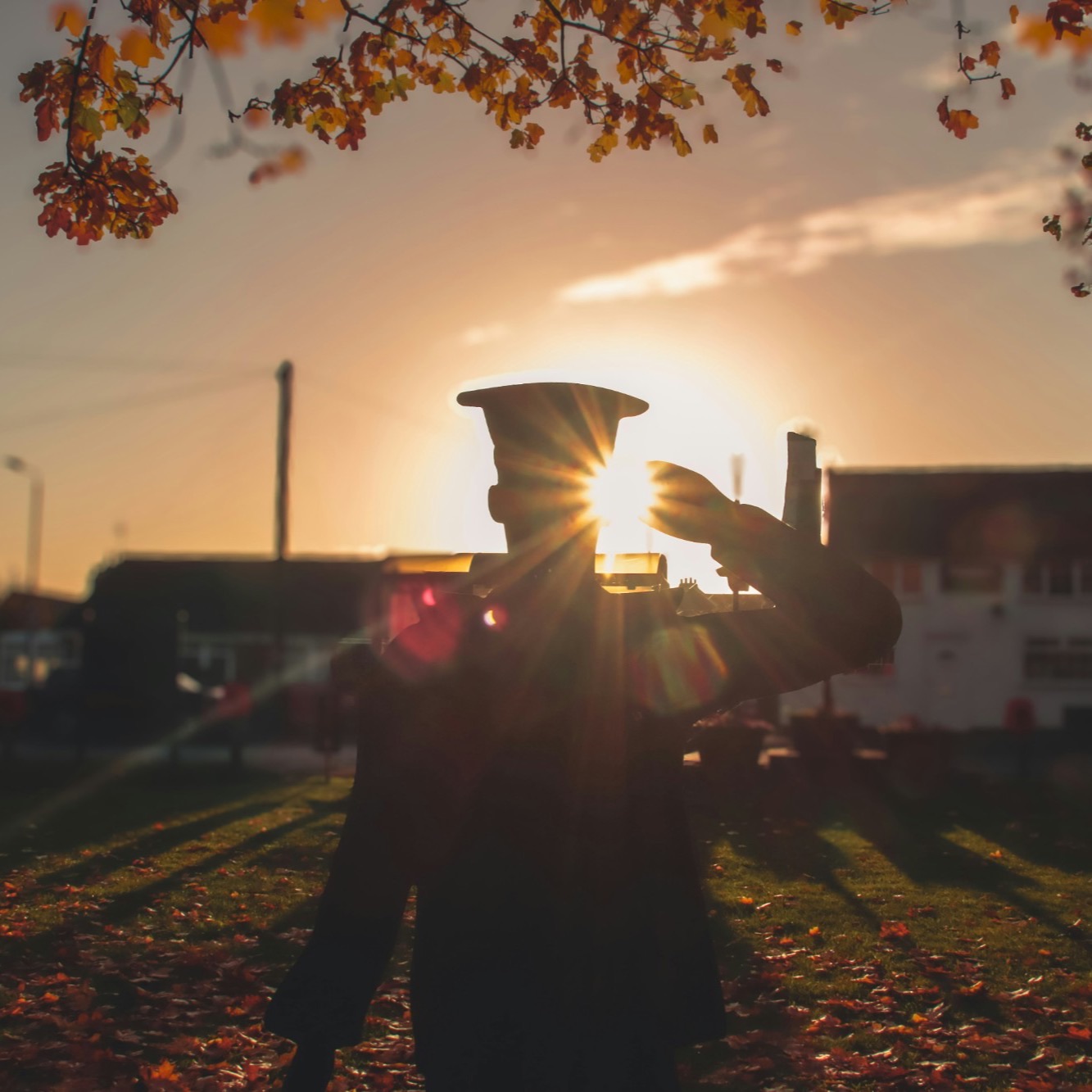 Silhouette of a saluting service member statue against a low sun, framed by autumn leaves