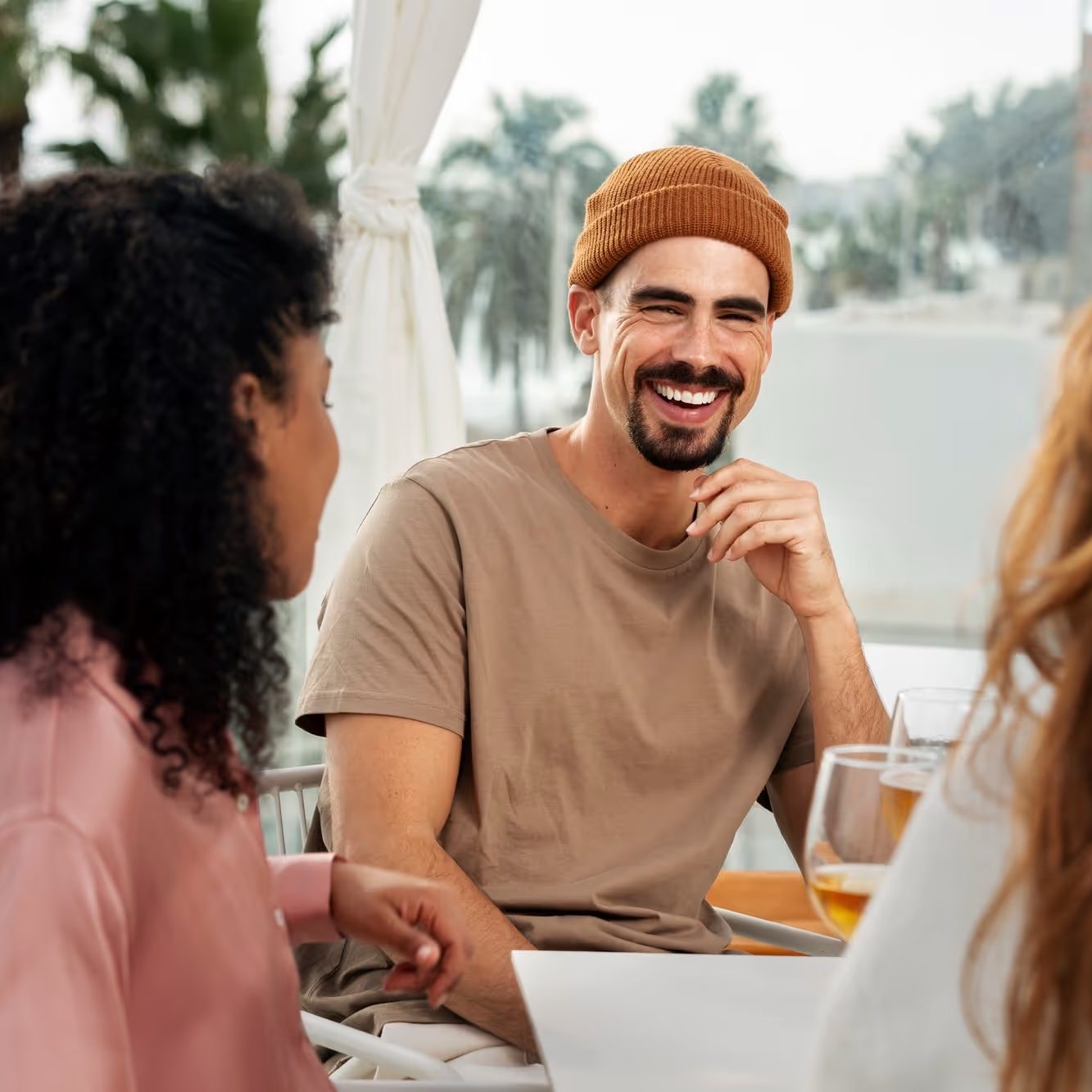A man in a beanie laughs with friends around an outdoor table