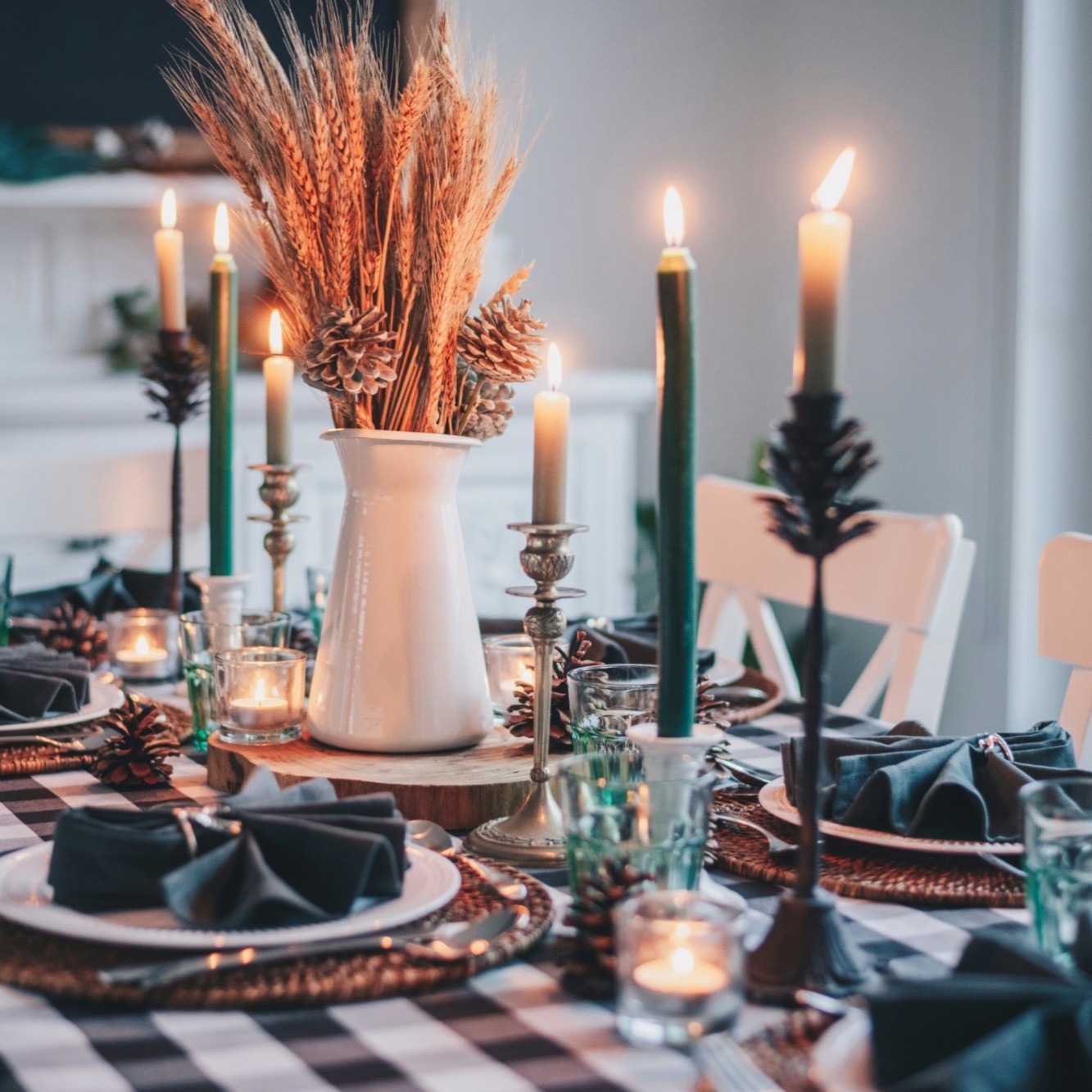 A candlelit Thanksgiving dinner table with wheat and pinecone centerpiece