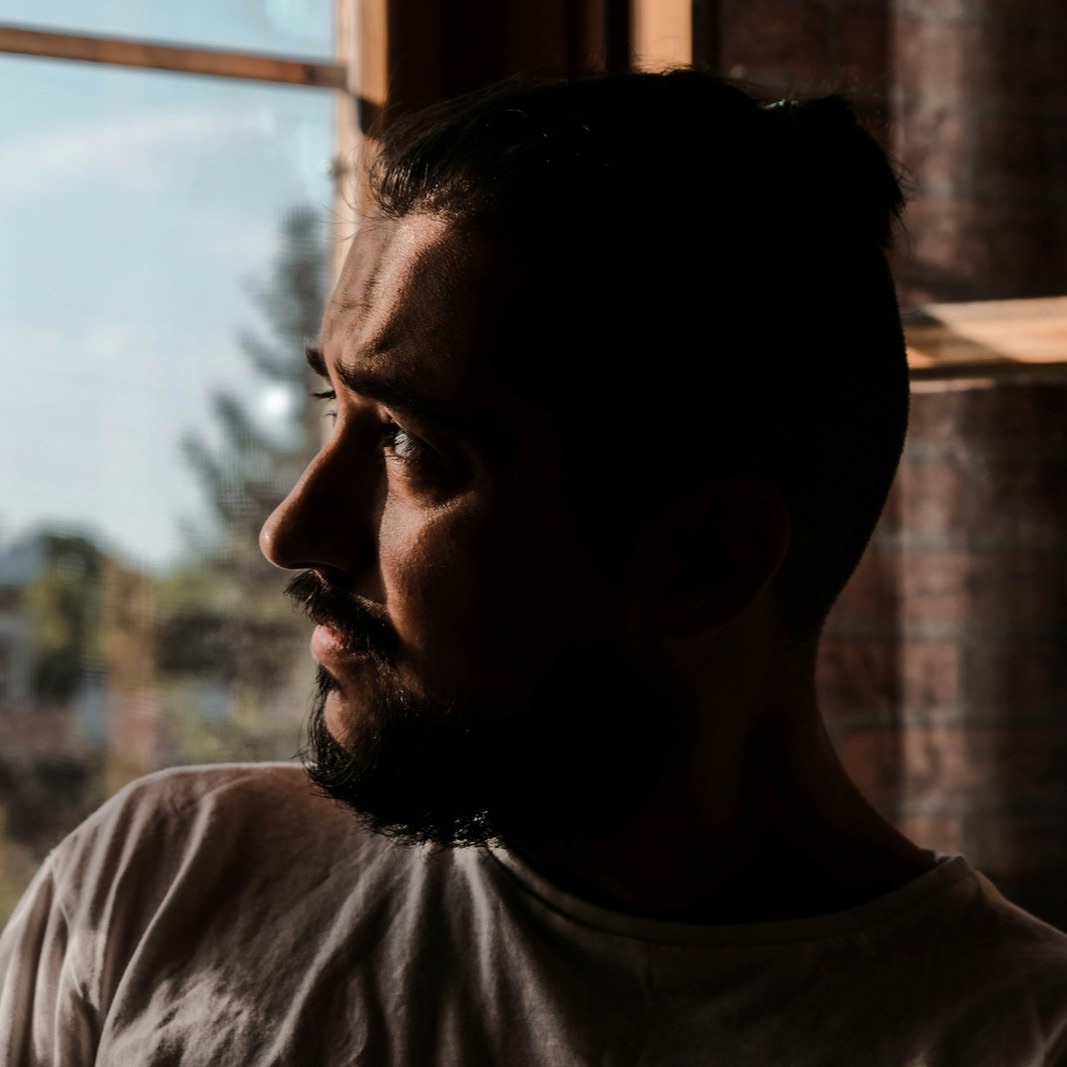 A man looks out a window in warm afternoon light, deep in thought